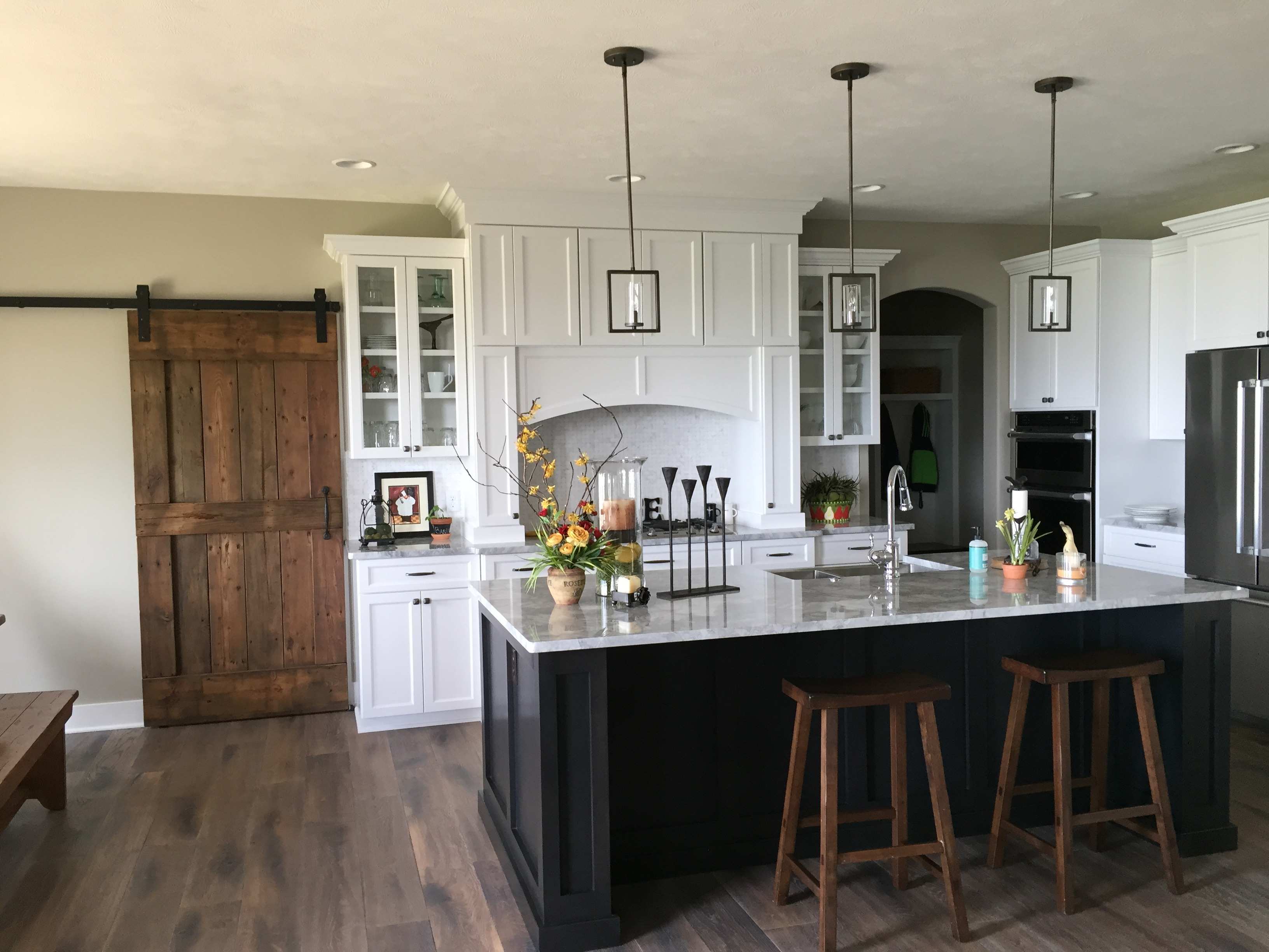 Custom kitchen with white cabinetry, dark island, and barn door